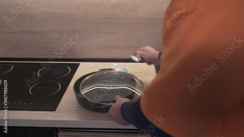 The man's hands screw the handle off the pan lid after washing.