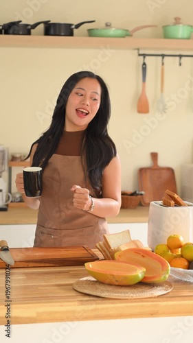Happy woman dancing while preparing healthy breakfast in a cozy kitchen, enjoying morning routine.