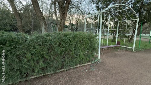 Wallpaper Mural A peaceful wooden bench sits tucked inside a white metal frame in Vorontsov Park. Dense green hedges and tall trees surround the area, creating a quiet and cozy spot for morning reflection. Torontodigital.ca