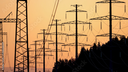 Silhouettes of power lines stretch across golden sunset sky