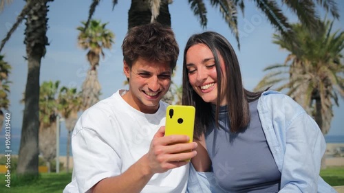 Happy young couple enjoying a delightful moment together as they share laughter while viewing something on their smartphone, showcasing their connection and happiness with each other.