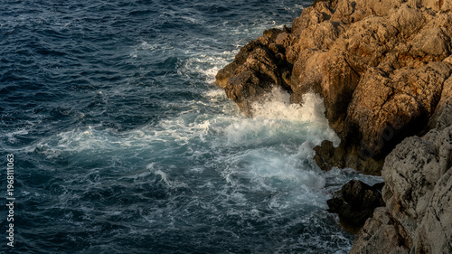 Foto Waves Crashing Against Sunlit Rocky Coastline