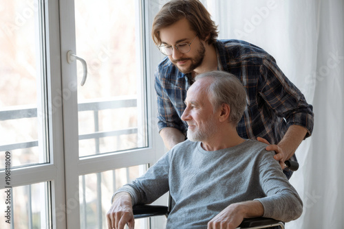 Adult son assisting elderly father in wheelchair near window, medium close-up, bright home interior, emotional family support moment