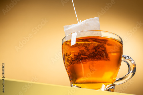Glass cup of tea with tea bag inside on yellow background