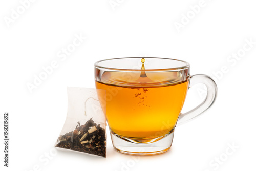 Glass cup of tea with splashing droplet and tea bag, isolated on white background.