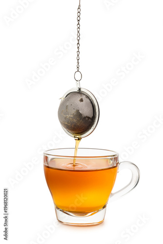 Glass cup of tea with dripping metal tea infuser, isolated on white background.