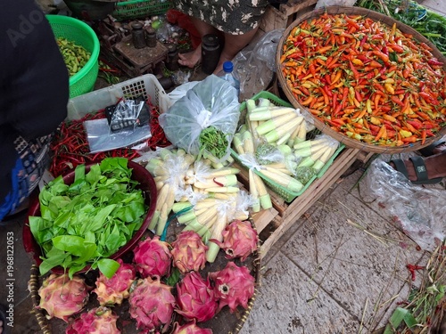 The atmosphere at a traditional market selling a variety of agricultural products and fruits. Bird's Eye Chili: A pile of red and orange bird's eye chilies, a popular spice in Southeast Asia. 