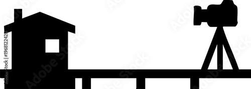 Silhouette of house and camera on tripod on wooden platform against checkered background.