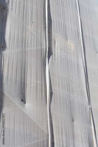 A detailed close-up shows the textured surface of a white protective netting covering a building facade, with some creases and shadows