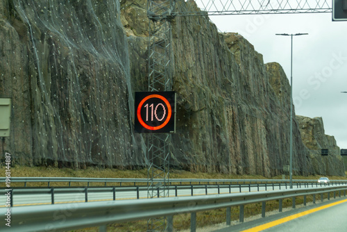 Fotografie Digital 110 Variable Speed Limit Sign on Modern Norway Motorway with Rocky Cliff