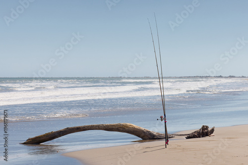 Foto Two long surf fishing rods placed upright in sand holders on a wide sandy ocean beach