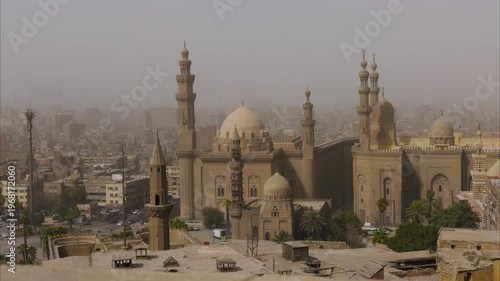 Aerial view of Sultan Hassan and Al-Rifai mosques with minarets and domes in dusty haze from Cairo Citadel, Egypt. Atmospheric Islamic architecture for travel and history.