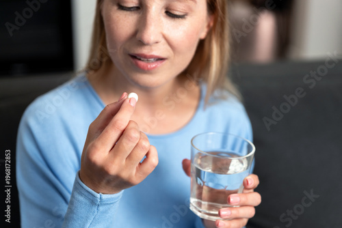 Young woman prepares to take medication with water at home in the living room