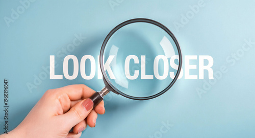 Close Up Of Hand Holding Magnifying Glass Over Look Closer Text On Light Blue Background Concept Image