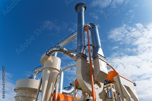 Industrial air filtration and cyclone dust collector system at a grain processing facility, heavy duty ventilation pipes and agricultural machinery under blue sky