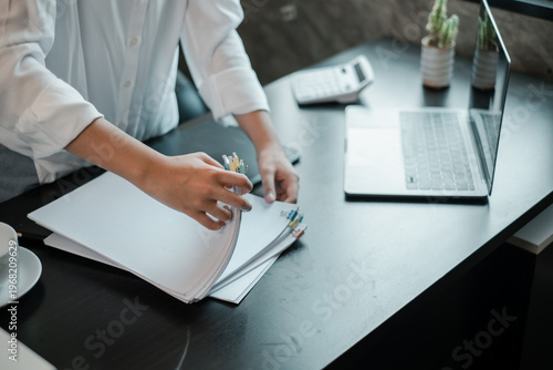 Business Professional Organizing Documents at Modern Office Desk with Laptop and Calculator