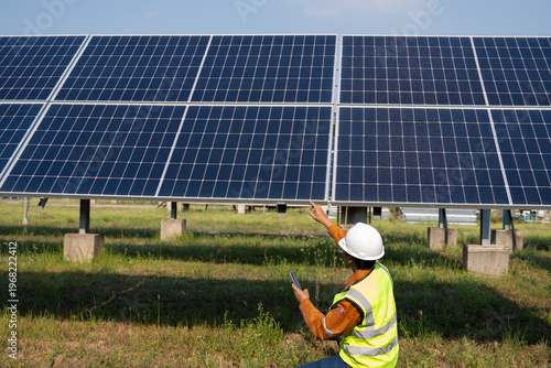 Field technician checking ground-mounted photovoltaic panels, using handheld device while adjusting array alignment, ensuring stable performance and efficient energy generation in outdoor conditions.