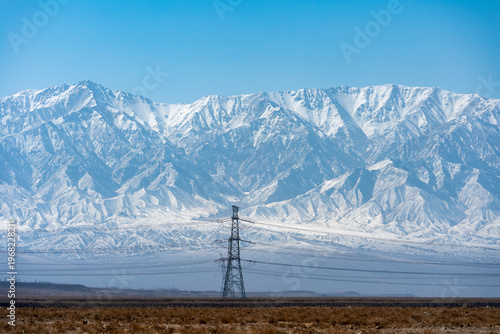 Fotografía Snow covered Qilian Mountains in China with power lines in the foreground under