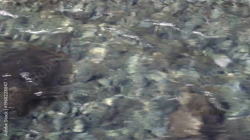 Fast river current flowing over dark rocks and small gravel