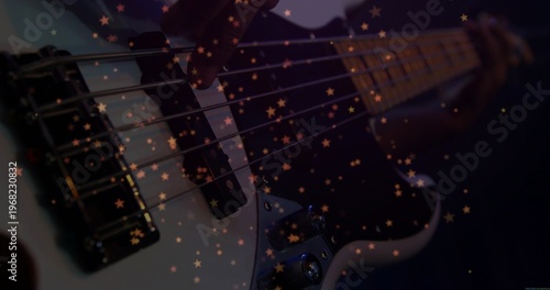 Plucking musician's hand in dark sleeve moving along bass guitar strings at studio, with star bokeh