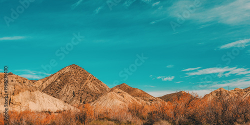 Arid mountainous semi desert landscape with vegetation under a blue sky with some thin clouds. Desierto de Tabernas, Almeria, Andalusia, Spain.