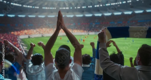 Back view Soccer Supporters Celebrate in a Packed Stadium, Raising hands andDuring a Professional Worl Championship Match, as the Crowd Roars Around the Field. Big Euro Event