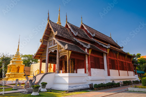 The beautiful Viharn Lai Kham and golden pagoda of Wat Phra Singh under a clear blue sky, showcasing exquisite Lanna style architecture in Chiang Mai, Thailand.