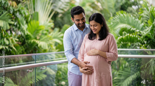 Expectant Indian couple smiles, husband holds wife's pregnant belly.
