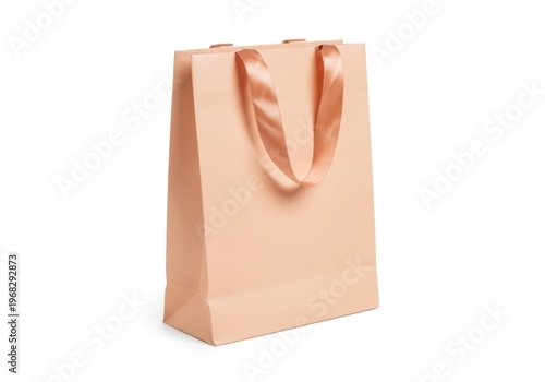 Empty peach colored paper shopping bag with satin ribbon handles isolated on white background