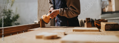 Konstfotografi A carpenter uses an orbital sander to smooth a wooden plank on a workbench