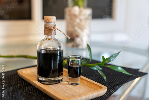 Tableau sur toile Glass bottle and shot glass with dark coffee liqueur on a wooden tray