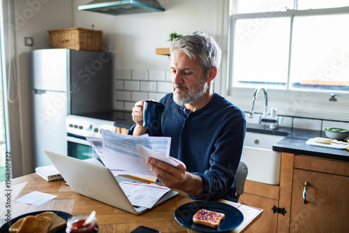 Mature man paying household bills at kitchen table