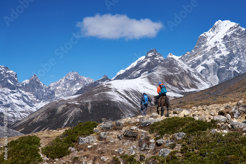 Breathtaking view of snow-capped Himalayan range under a bright sunny sky, with two trekkers on Everest Base Camp trail 
