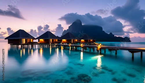 Luxury villas on stilts over crystal-clear turquoise ocean water with distant mountain at dusk.