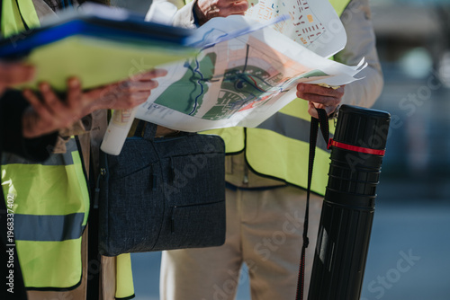 Schilderij op canvas Construction engineers review site plans and maps while wearing high-visibility safety vests