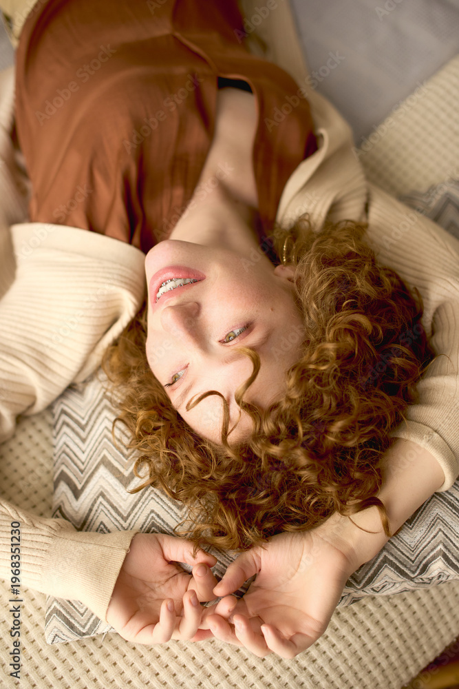 Obraz premium Curly young woman relaxing in her modern beige apartment with a joyful smile