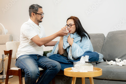 A young woman with a fever rests while her husband takes care of her, expressing love, support, and family care during illness.