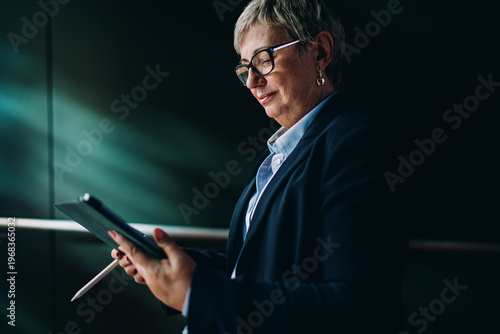 Schilderij op canvas Senior woman in formal attire interacting with tablet and stylus, reflecting digital literacy, tech empowerment, and concentration in mobile business workflows