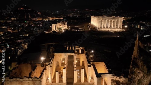Aerial drone cinematic night video of iconic illuminated Propylea or gate of Acropolis hill and the Parthenon, Athens historic centre, Attica, Greece