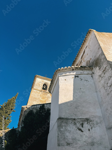 Old white church with pine tree under a clear blue sky. Colmenar, Malaga, Andalusia, Spain.