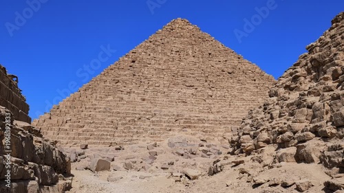 Close-up view of Pyramid of Menkaure with subsidiary pyramids and ancient stone ruins at Giza, Egypt. Massive limestone blocks against vivid blue sky. Travel and history.
