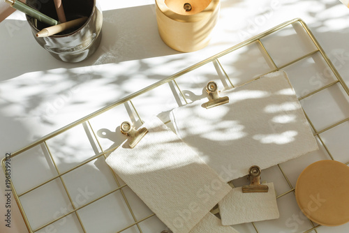 Minimalist wall organizer with brass clips, paper mockups, and ceramic decor in natural light.
