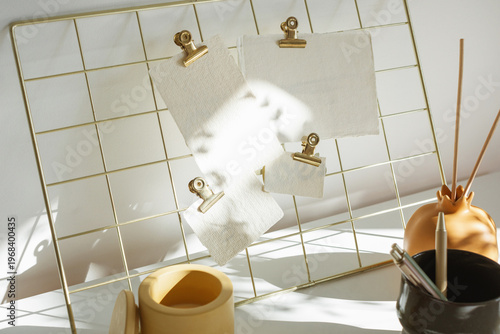 Creative workspace featuring a metal grid board with brass clips, paper sheets, and ceramic decor in natural light.