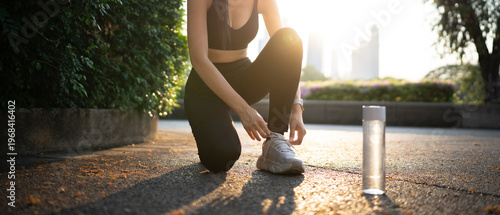 Fotografía Strong athletic girl in sportswear and water bottle ob floor tying shoelaces on