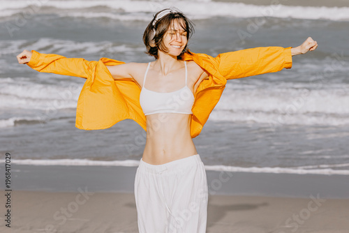 Young woman stretching arms with headphones on sandy beach shoreline