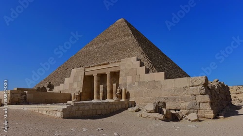 Pyramid of Khufu with restored mortuary temple entrance, pharaoh statues and columns at Giza, Egypt. Rare view of pyramid complex against vivid blue sky.