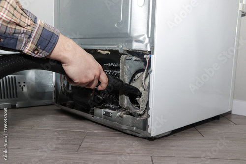 Foto Male hand vacuuming refrigerator condenser and internal components after removing back cover