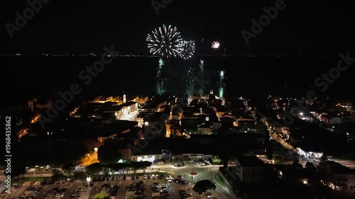 Aerial view of Lazise historic center during Garda fireworks 2025. Drone video captures lakeside town, medieval streets, and vibrant evening lights in summer.