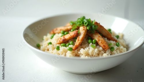 White bowl holds seasoned rice topped with grilled chicken slices, bright green peas, fresh spring onions. This tasty meal offers visually appealing, balanced dish, perfect for any dining occasion.