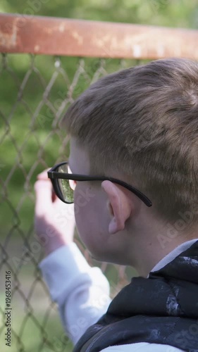 Sad teenage boy near fence after school, theme of bullying. Vertical video.